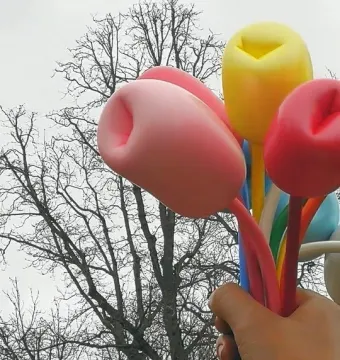 Bouquet of Tulips sculpture with a hand holding pink, yellow, and red tulips against bare tree branches and an overcast sky.
