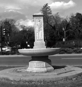 Butt–Millet Memorial Fountain standing in a grassy median with a tall rectangular stone shaft and circular basin