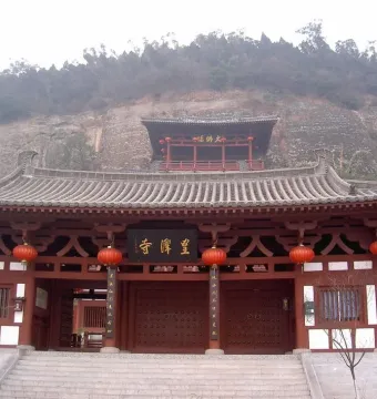 Huangze Monastery entrance with red columns, hanging lanterns, and a stone staircase against a rocky mountainside.