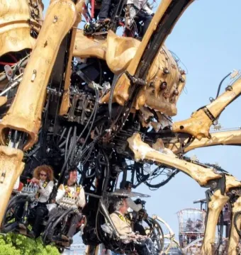 La Princesse, a giant mechanical spider, with people seated in platforms beneath its body against a blue sky.