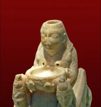 Lady of Galera figurine showing a seated carved figure holding a basin, flanked by two smaller winged figures.