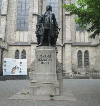 Bronze statue of Johann Sebastian Bach on a stone pedestal in front of a gothic stone building.