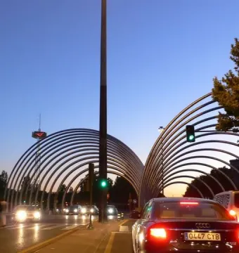 Puerta de la Ilustración arches over a road in Madrid at twilight, with cars passing underneath.