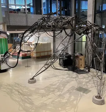 The Senster sculpture with an arched skeletal metal frame, three legs, and cables draped across its structure.