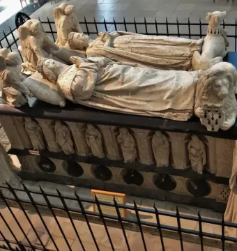 The Tomb of Francis II of Brittany with two recumbent crowned effigies, surrounded by carved figures and enclosed by a black metal fence.
