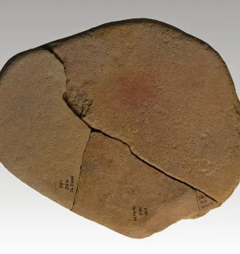 Reddish-brown stone fragment from the Venus of Monruz, with a prominent crack and faint black markings.