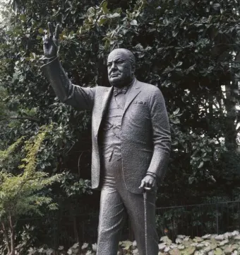 Winston Churchill statue holding a cane and raising a V sign outdoors.