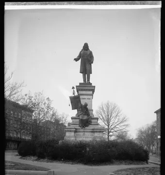Albert Pike Memorial showing a bearded man in a long coat atop an ornate stone pedestal with a seated figure below and bare trees around it.