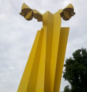 Ángel Custodio, a tall yellow abstract sculpture with wing-like forms at the top against a cloudy sky.