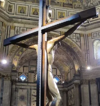Brunelleschi Crucifix displayed in a decorated church interior with visitors gathered below.