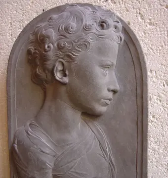 Bust of a Child in gray stone, shown in profile with curly hair and draped shoulders.