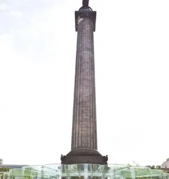 Melville Monument rises above St Andrew Square Gardens beside a modern glass pavilion, with three women looking up in the foreground.