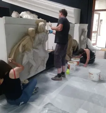 Workers restoring large Parthenon metopes in a studio filled with plaster casts.