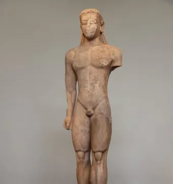 Sounion Kouros marble statue with missing right arm and eroded face, standing on a stone plinth in a museum.