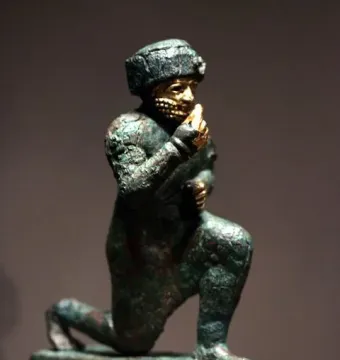 Worshipper of Larsa kneeling figure with a raised hand and gold details on an oxidized green surface.