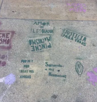 Concrete sidewalk covered with green and purple stencil graffiti in Spanish, including feminist slogans and symbols, near the Antimonumenta.