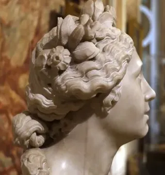 Blessed Soul marble bust in profile, with curled hair and floral details on a reddish-brown pedestal.