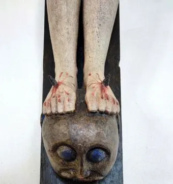 Close-up of the Enghausen Cross showing the nailed feet of the crucified figure resting on a carved head with blue eyes.