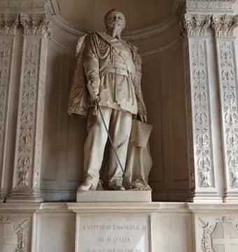 Monument to Vittorio Emanuele II showing a marble statue of a man in military uniform holding a sword and a document above an inscribed pedestal.