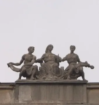 Music sculpture with three seated figures on a rooftop in Warsaw, including a central woman with outstretched hands and a woman holding a stringed instrument.