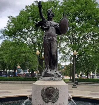 Russell Alger Memorial Fountain with a bronze draped female figure holding up an arm and shield atop a stone pedestal.