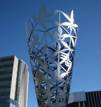 The Chalice metal sculpture rising against a blue sky in Christchurch, with modern buildings behind it.