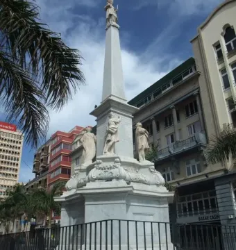 The Triumph of the Candelaria monument, a white stone obelisk with carved figures at the base and a statue on top, in a city square