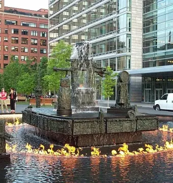 La Joute bronze fountain with water cascading from the center and flames burning on the surrounding pool.