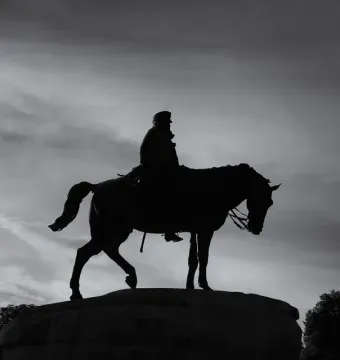 Silhouette of the Monument to General Martínez-Campos, an equestrian statue on a stone base against a cloudy sky.
