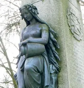 Mutter Kinzig statue of a bronze-colored woman holding an urn beside a stone monument
