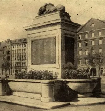 Sleeping Lion sculpture resting atop a stone monument with its head lowered and turned slightly.