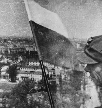A soldier stands beside a two-toned flag with the Victory Column overlooking Berlin.