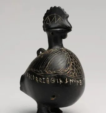 Viterbo Rooster, a dark bird-shaped vessel with etched feather patterns and an inscription around the lower body.
