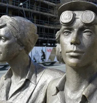 Close-up of two figures from the Women of Steel sculpture, one wearing a cap with goggles on the brim.
