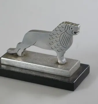 Silver-colored metal lion figure on a two-tiered rectangular base, facing right.