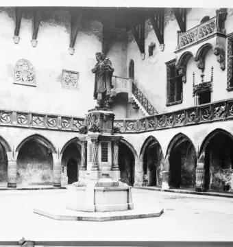Copernicus Monument on a pedestal in a historic courtyard with arched arcades.