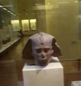 Djedefre sphinx head displayed on a pedestal behind glass in a museum gallery.