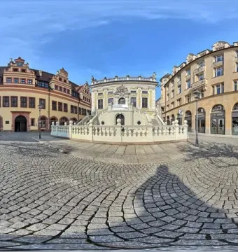 Goethe Monument on a reddish-brown pedestal beside a cobbled square in Leipzig.