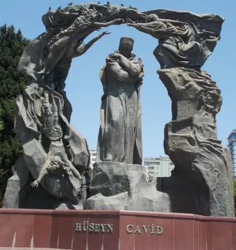 Huseyn Javid monument with a central robed figure, flanked by tall sculptural forms and arching figures above a red stone base.