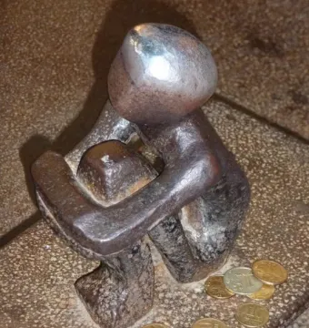 Järnpojke, a small dark metal seated figure hugging its knees, with coins scattered around the base.