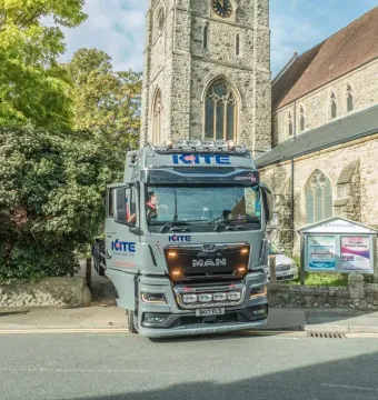 A large KITE Haulage Ltd truck parked on a street beside a stone church with a tall clock tower.