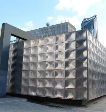 Michael Faraday Memorial with reflective stainless steel panels and dark support beams against a blue sky.