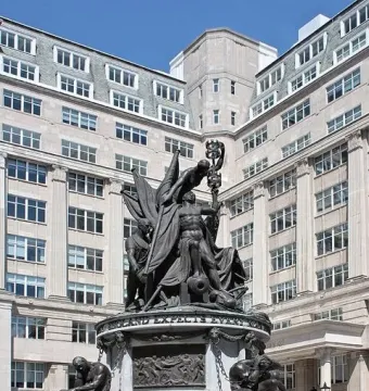 Nelson Monument in Liverpool with bronze figures on a stone base beside a tall stone building.