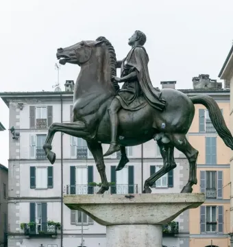 The Regisole equestrian statue stands on a stone pedestal in a city square in Pavia.