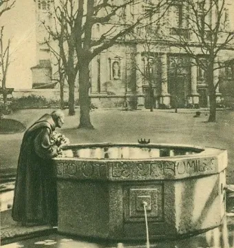 Sepia-toned view of the Saint Francis Fountain with a robed figure leaning over the carved stone basin as water flows into the lower pool.