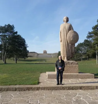 The Ghosts sculpture with a robed figure holding a circular shield, with a person standing on the stone path nearby.