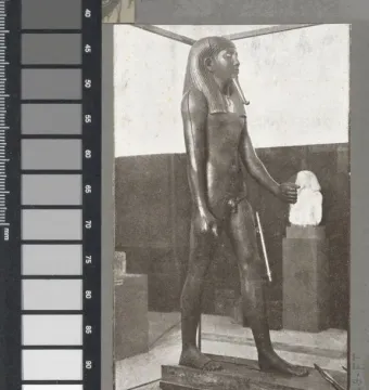 Standing statue of King Hor with a headdress and broad collar, shown stepping forward on a rectangular base.