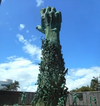 The Miami Beach Holocaust Memorial features a towering bronze hand rising above clustered human figures and scattered sculptures in a plaza.