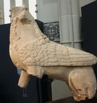 Weathered stone Sphinx of Agost sculpture with missing head and one foreleg, shown on a museum stand.