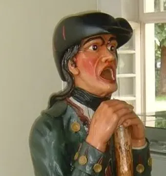 Aschaffenburger Maulaff, a painted wooden figure in a green coat and dark cap, leaning on a staff with its mouth open.